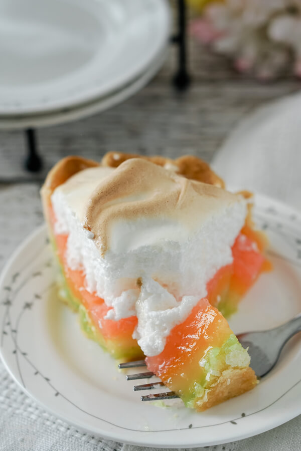 A bite of rainbow lemon meringue pie rests on a fork, showing the layers of colored filling. 