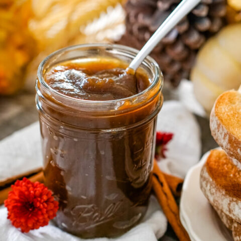 A jar of homemade pumpkin butter with a spoon in it sitting next to a plate of toast.
