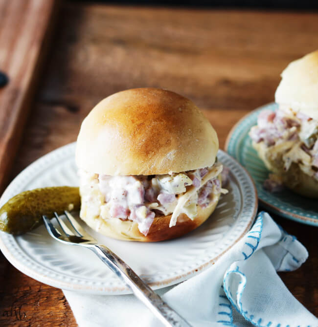 A slider bun filled with cuban ham salad on a plate with a dill pickle next to it. 