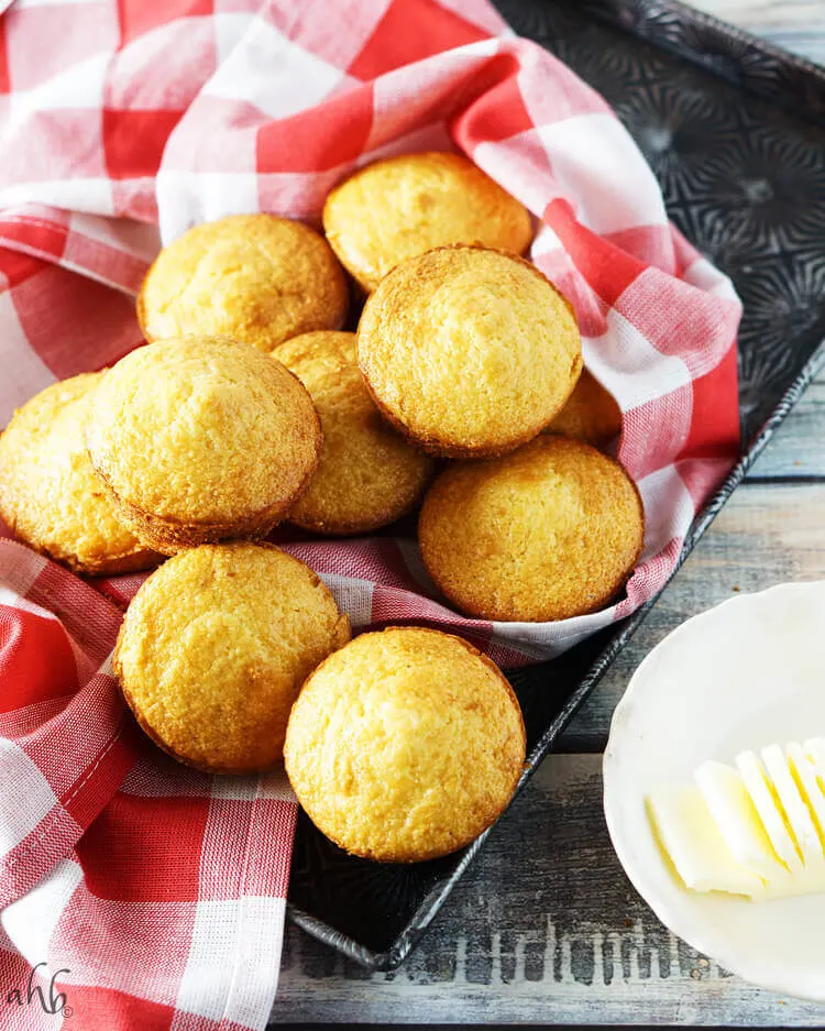 A tray of baked corn muffins next to a stick of butter.
