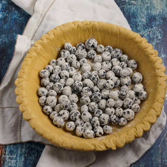 Flour dusted blueberries are added to the pie crust. 