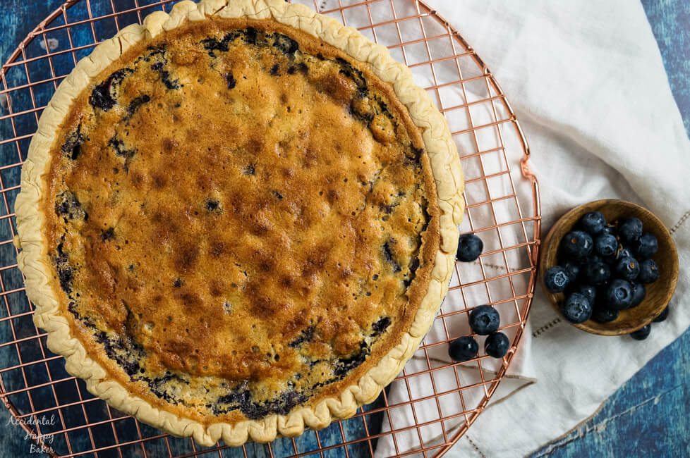 A fresh baked blueberry buttermilk pie rests on a cooling rack.