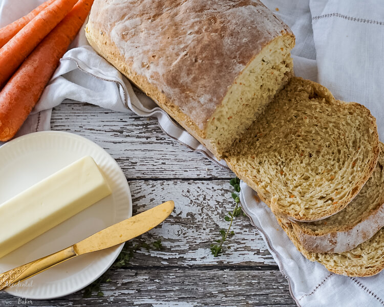 Freshly sliced carrot and chive bread next to a plate with bread and butter.