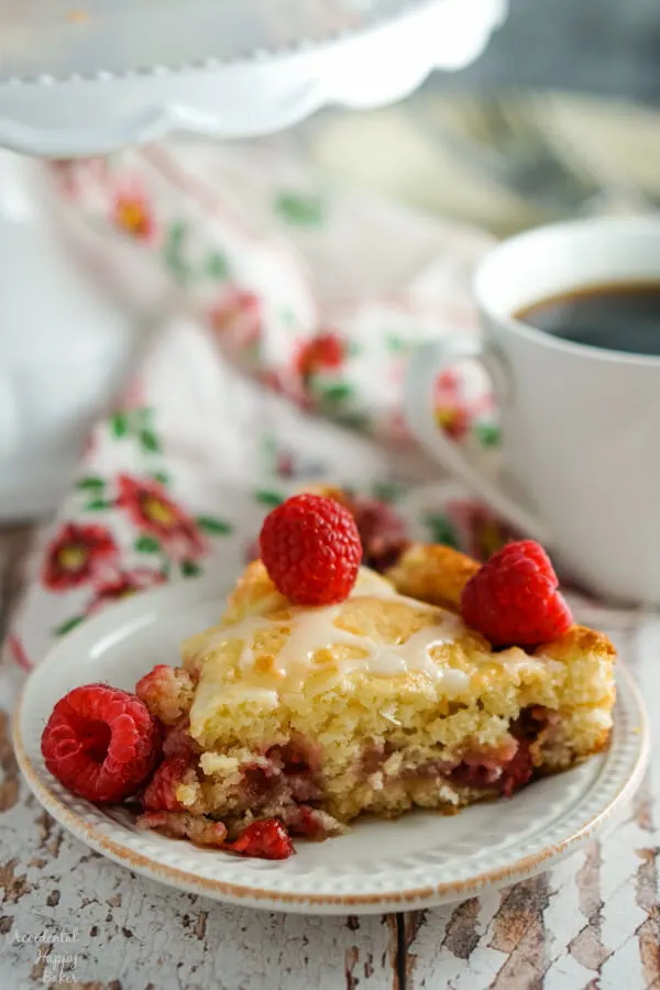 A slice of raspberry coffee cake sitting next to a cup of coffee.