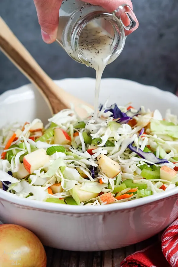 A homemade poppy seed dressing is poured over the apple coleslaw