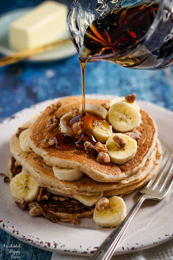 Maple syrup is poured over a stack of banana pancakes. 