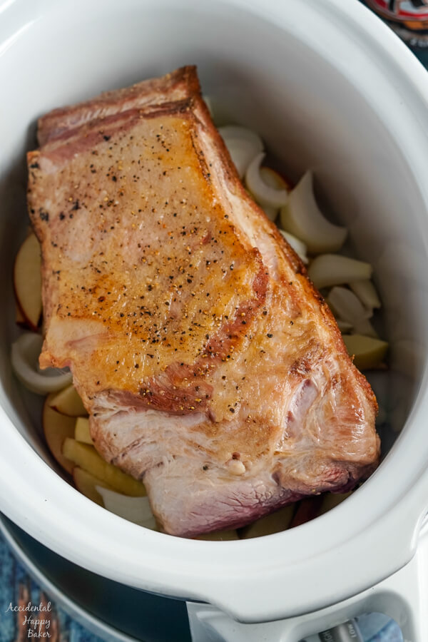 Seared Boston Butt Roast is placed on top of the apples and onions in the slow cooker. 