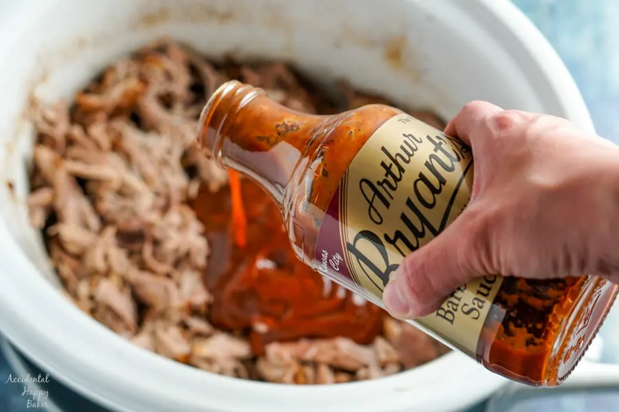 A bottle of barbecue sauce is added to the pulled pork. 