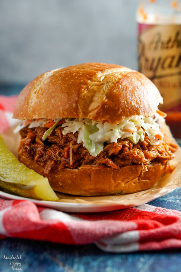 A pulled pork sandwich topped with coleslaw sitting beside a dill pickle. 