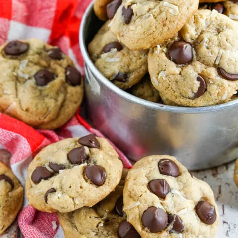 Chewy Coconut Chocolate Chip cookies stacked on a red checked towel and nestled in a metal bucket.