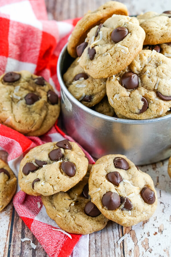 Chewy Coconut Chocolate Chip cookies stacked on a red checked towel and nestled in a metal bucket. 