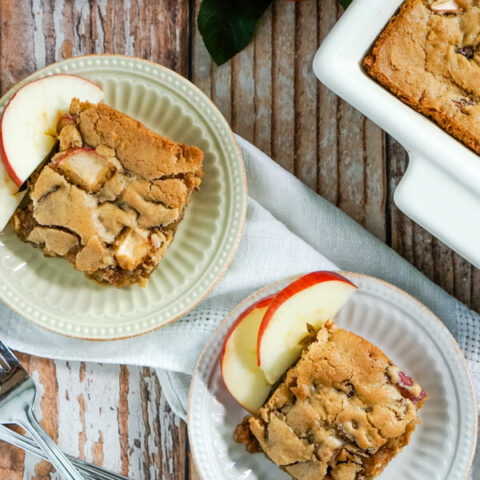 2 plates with slices of apple cinnamon bars sit next to two forks and a pan of apple cinnamon bars.