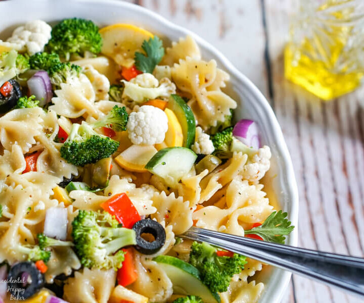 Summer vegetables and farfelle pasta tossed with an Italian dressing in a white bowl.