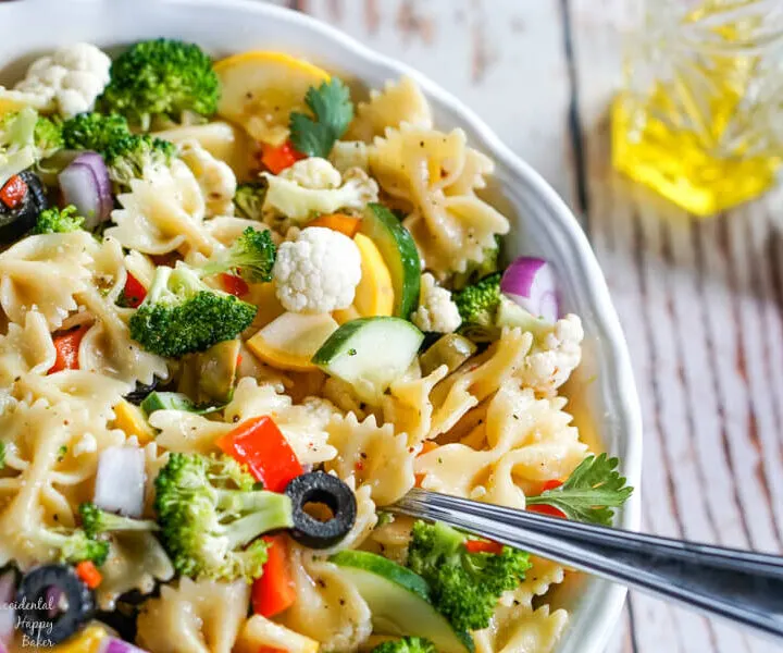 Summer vegetables and farfelle pasta tossed with an Italian dressing in a white bowl.