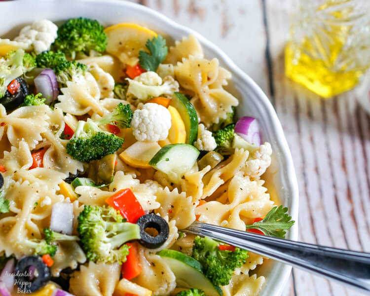 Summer vegetables and farfelle pasta tossed with an Italian dressing in a white bowl. 