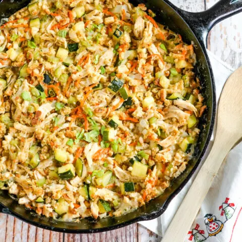 A cast iron skillet full of Chicken Zucchini Casserole sits next to a wooden spoon.