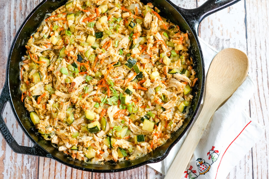 A cast iron skillet full of Chicken Zucchini Casserole sits next to a wooden spoon. 
