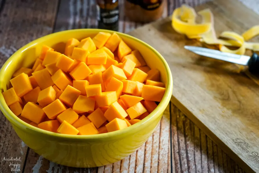 A yellow bowl of peeled and chopped butternut squash sits next to a cutting board and knife. 