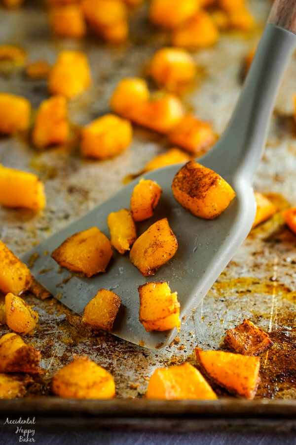 A sheet pan of cinnamon and bourbon roasted butternut squash with a spatula scooping up pieces of squash. 