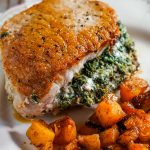A spinach stuffed pork chop on a white plate sitting next to some roasted butternut squash.