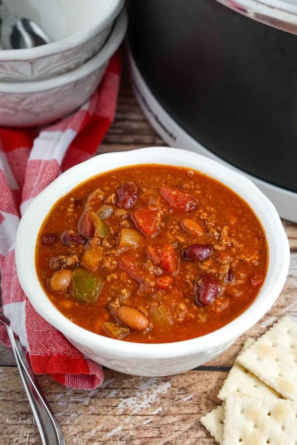 A white bowl of Wendy's copycat chili next to a slow cooker. 