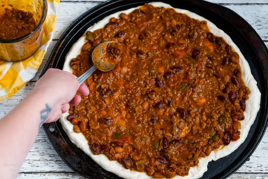 Chili is spread over the pizza dough for the sauce to Chili Dog Pizza. 