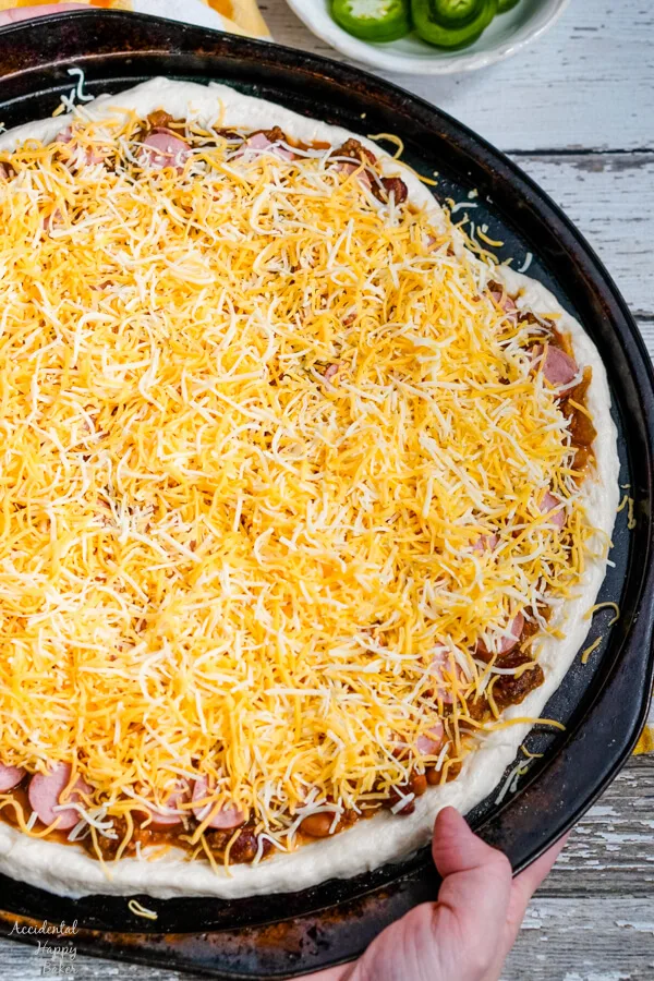 The chili dog pizza is topped off with shredded cheese. 