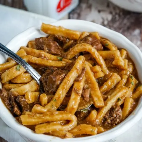 A white bowl full of Beef and Noodles sitting on top of a white cloth napkin.