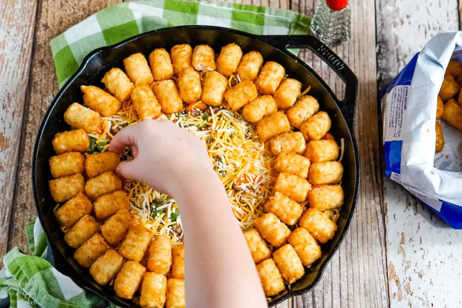 A layer of cheddar cheese is added before finishing the casserole with a layer of frozen tater tots. 