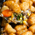A spoonful of Shepherd's Pie with Tater Tots is scooped out of the skillet.