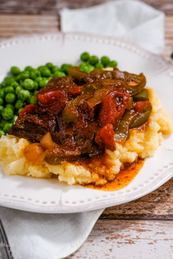 A serving of BBQ Swiss Steak on top of mashed potatoes on a white plate. 