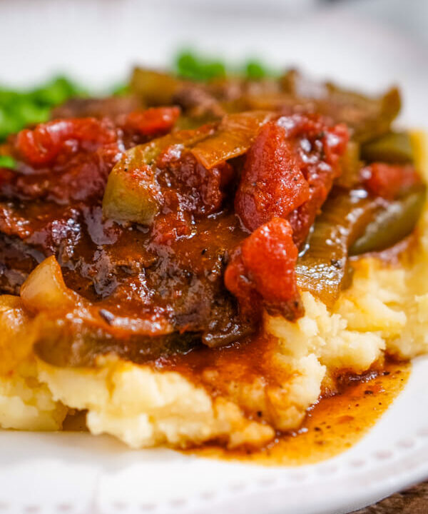 BBQ Swiss Steak with peppers and onions is served up on a pile of cheddar mashed potatoes.
