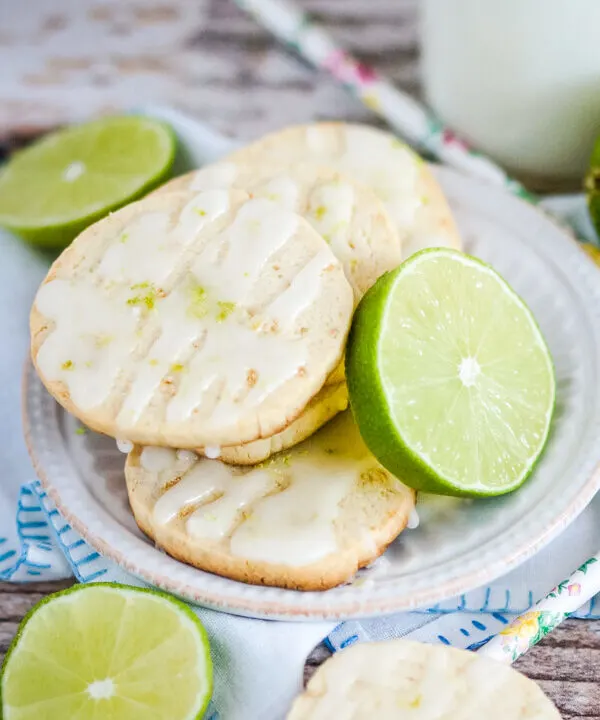 Key Lime Pie Shortbread Cookies stacked on a white plate with slices of lime.