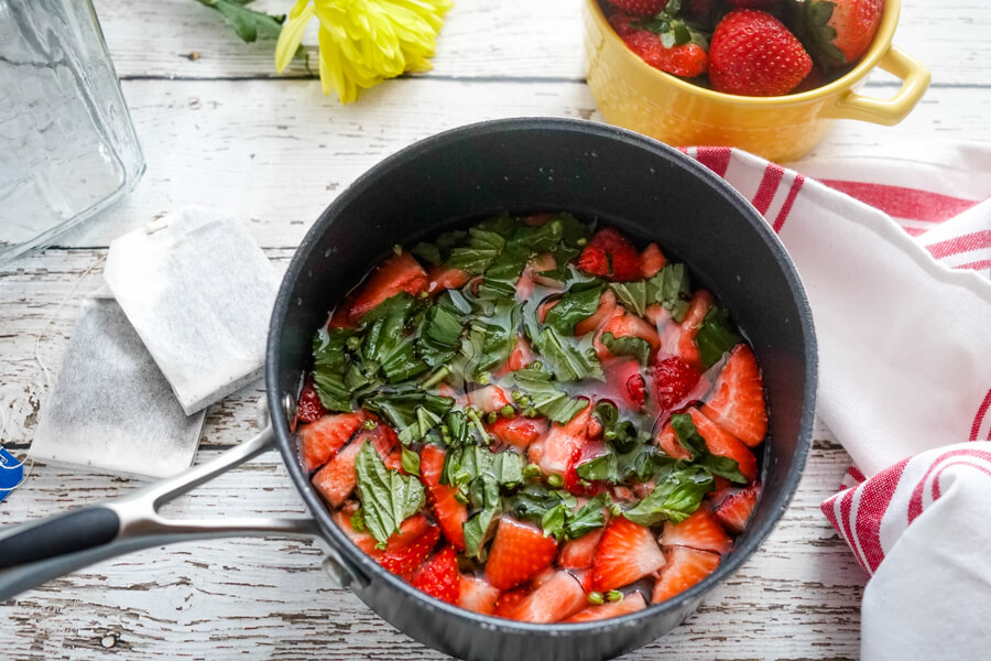 A small sauce pan with sliced strawberries and chopped basil. 