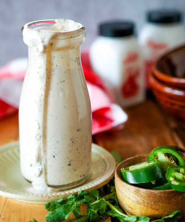 A bottle of dressing with cilantro to one side and a bowl of sliced fresh jalapeno peppers.