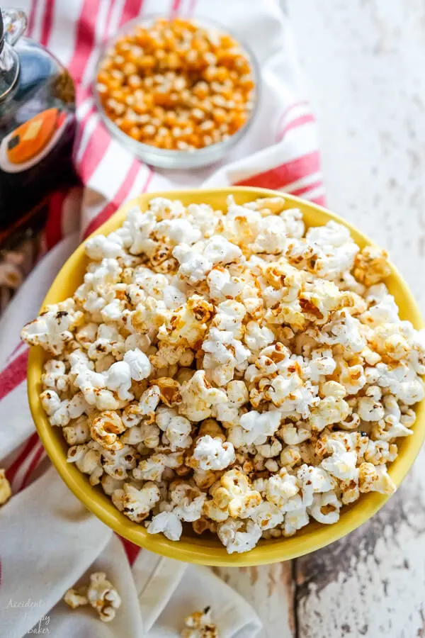 A bowl of kettle corn with some unpopped kernels and maple syrup in the background. 