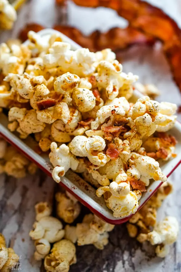 A close up image of a bowl of popcorn with bacon pieces and other seasonings. 