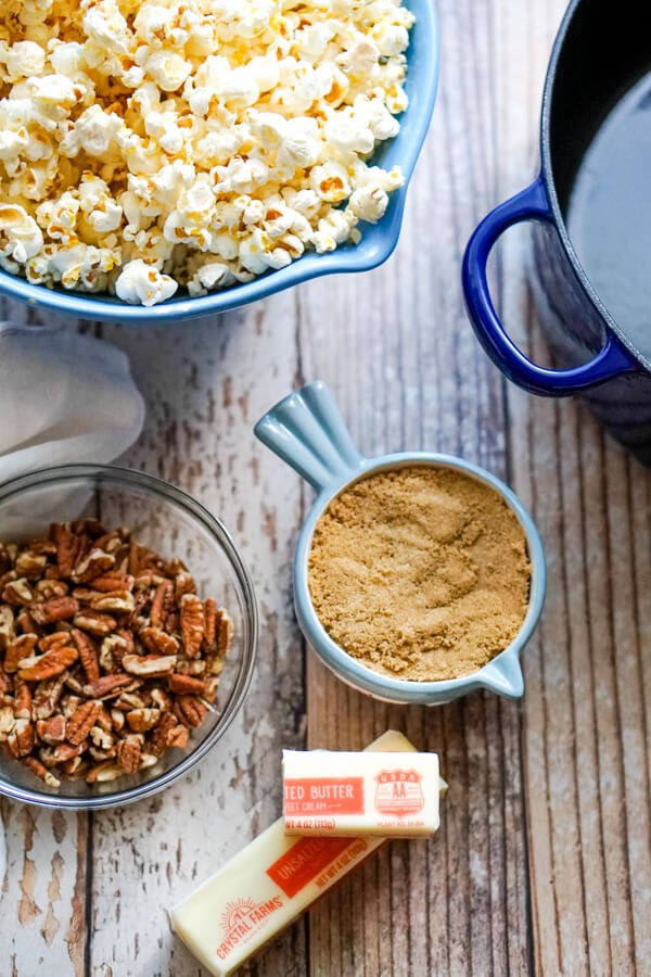 A bowl of popped popcorn next to pecans, brown sugar, and butter. 