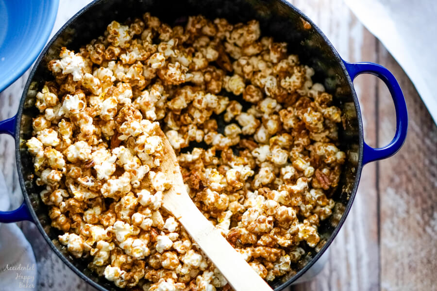 A blue dutch oven of caramel corn with a wooden spoon. 