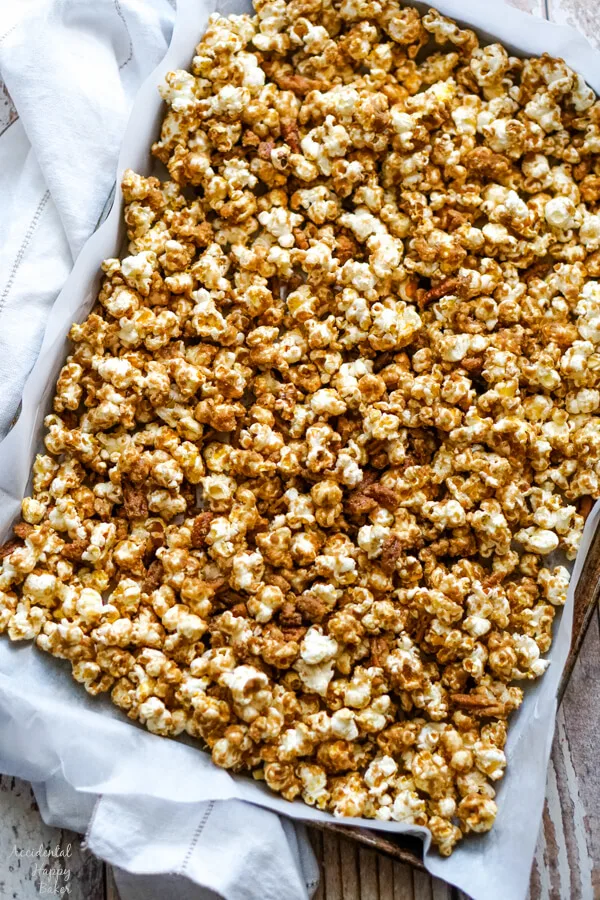The caramel corn is spread out on a lined cookie sheet to let cool. 