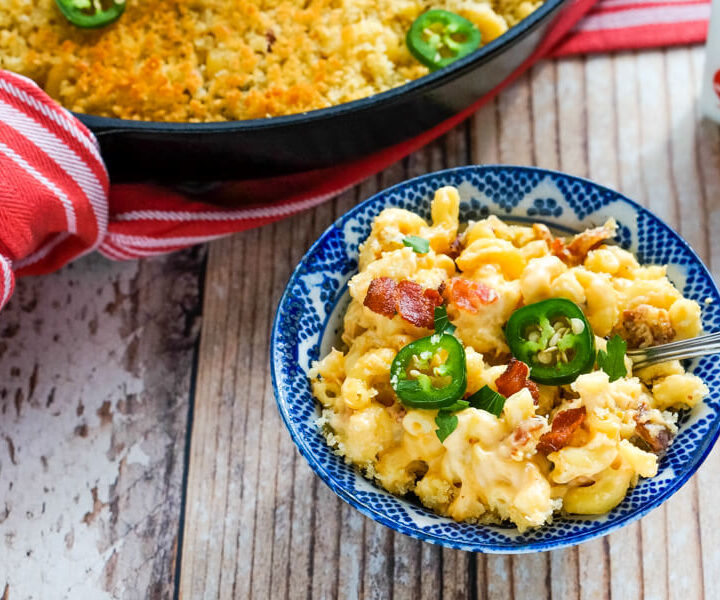 A blue and white bowl full of jalapeno bacon mac and cheese next to a skillet.