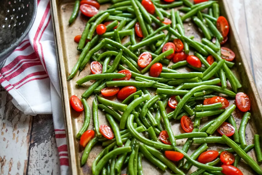 Green beans and tomatoes drizzled with olive oil and garlic on a sheet pan. 