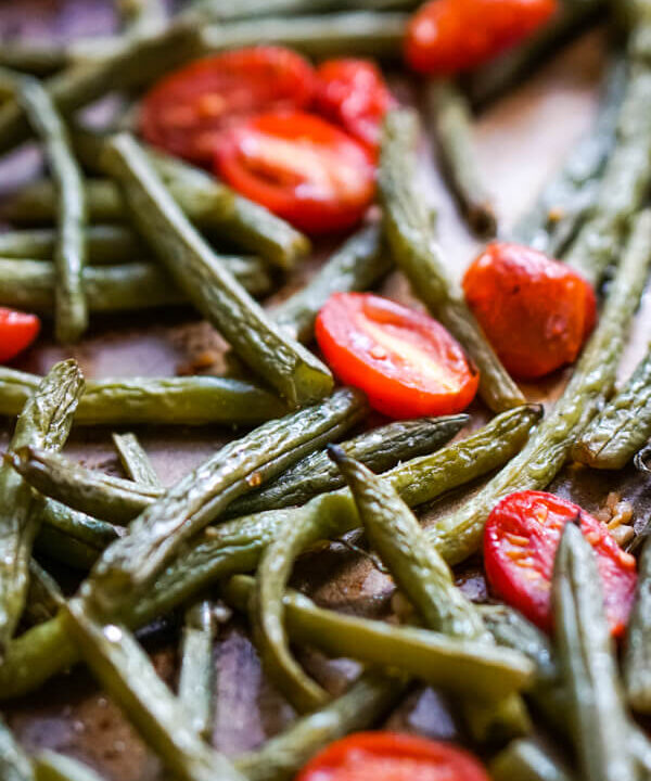 A close up image of a spatula scooping up a serving of roasted green beans and tomatoes.