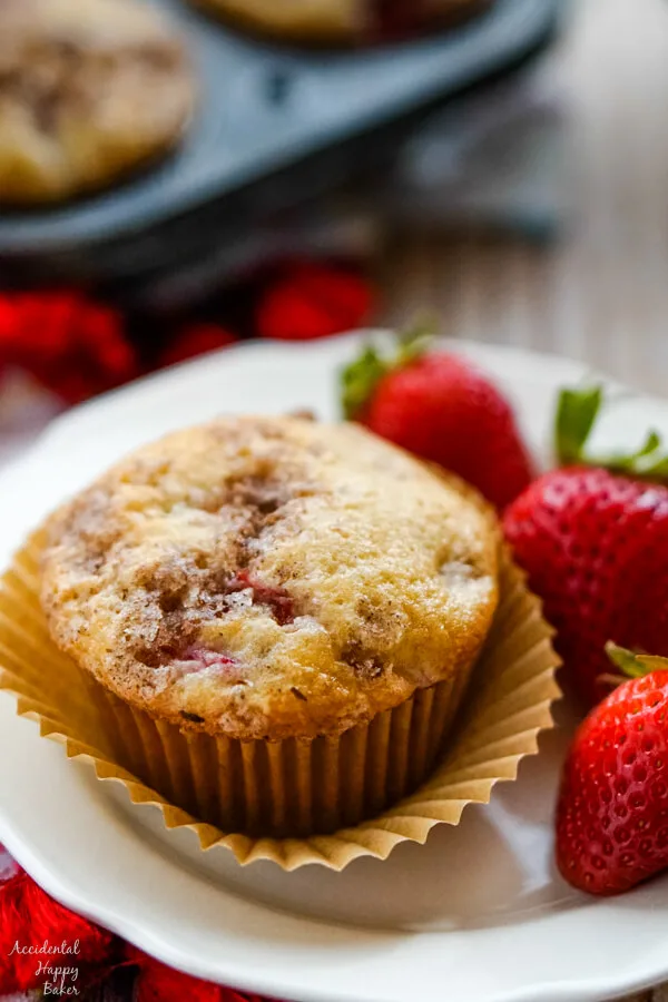 A strawberry rhubarb muffin on a plate with 3 strawberries. 
