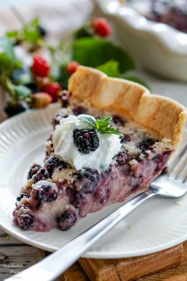 A slice of blackberries and cream pie on a white plate garnished with whipped cream, mint and fresh blackberries. 