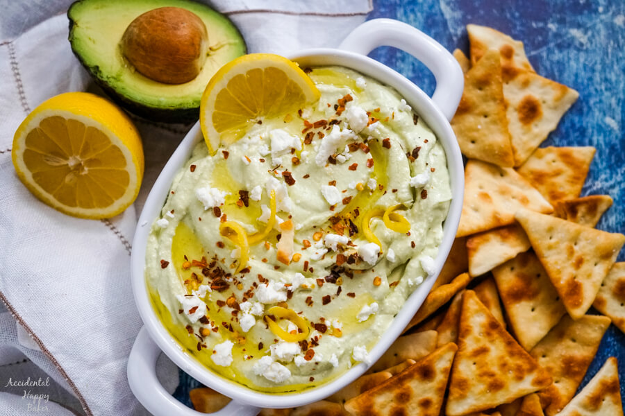 A white serving bowl of lemon feta dip surrounded by pita chips. 