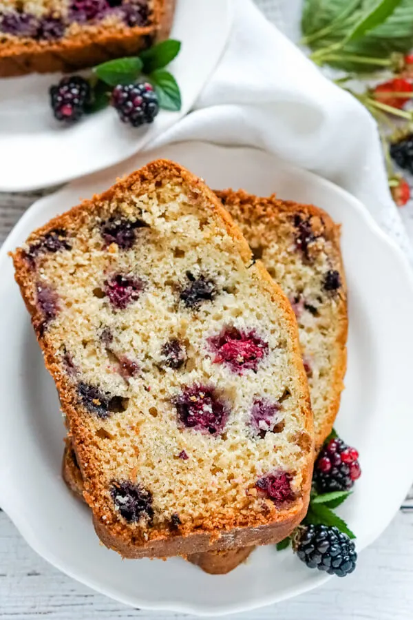 Two slices of blackberry bread on a white plate with fresh blackberries by the side. 