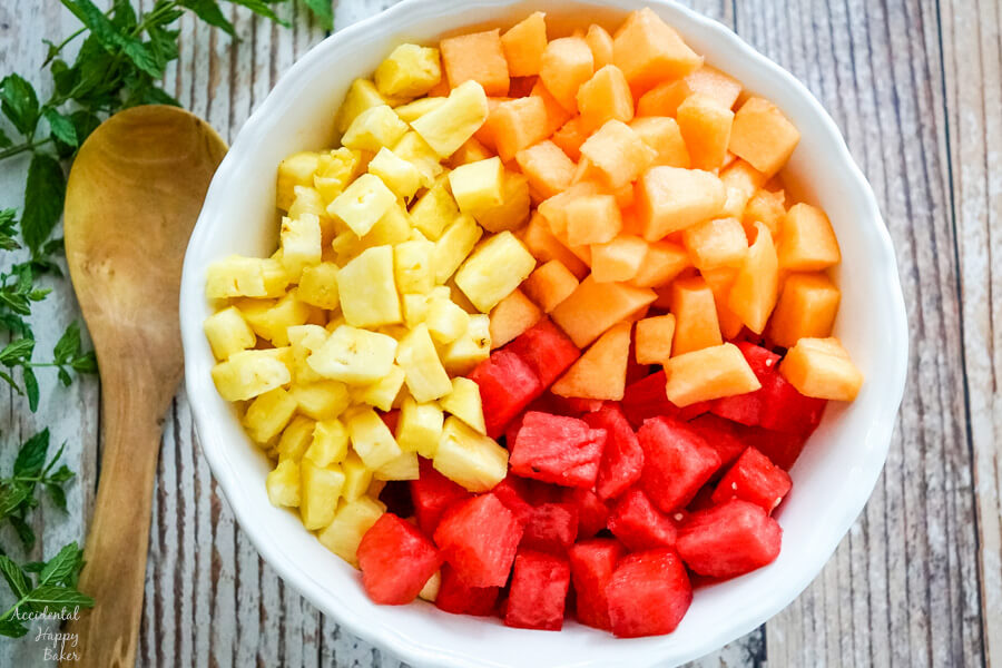 A large white bowl full of chopped watermelon, cantaloupe and pineapple