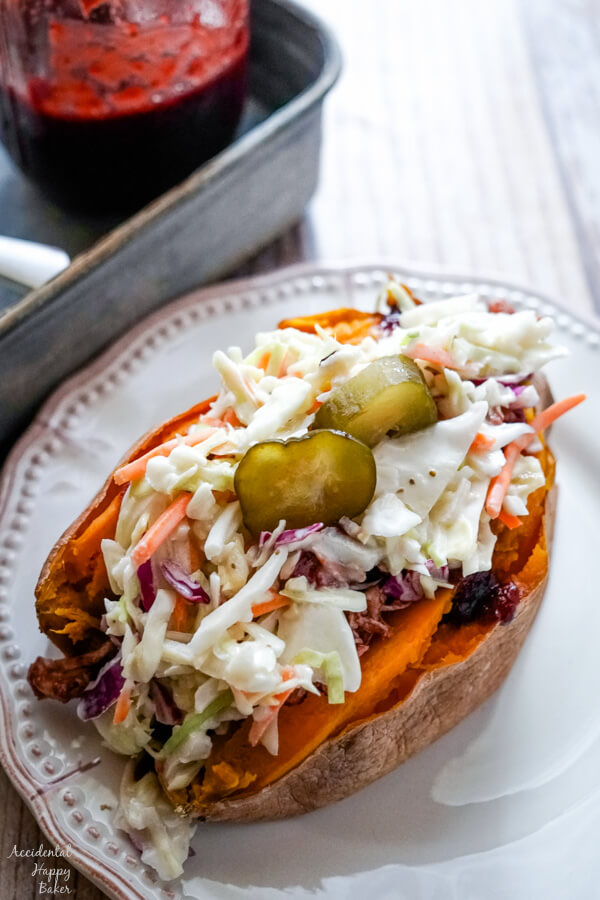A baked sweet potato stuffed with bbq chicken and coleslaw on a white plate. 