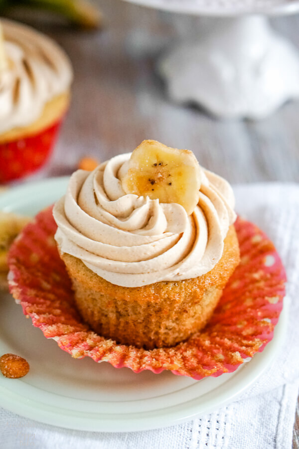 A close up image of a banana cupcake with peanut butter frosting accented with a banana chip on top. 